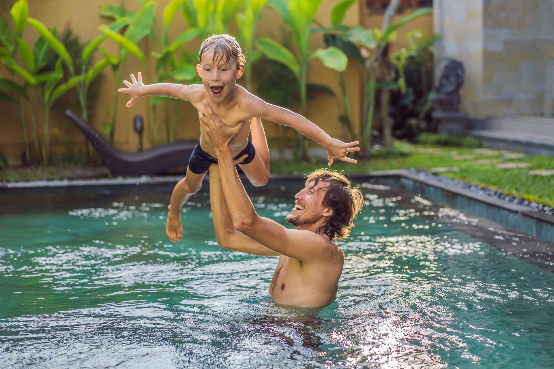 Vater hebt seinen lachenden Sohn im Pool hoch.