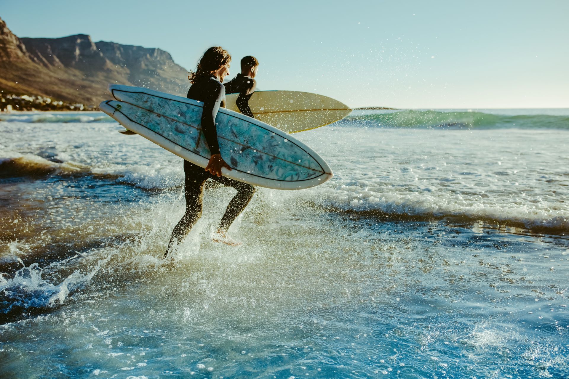 Zwei Surfer laufen mit Brettern ins Meer, bereit für die Wellen.