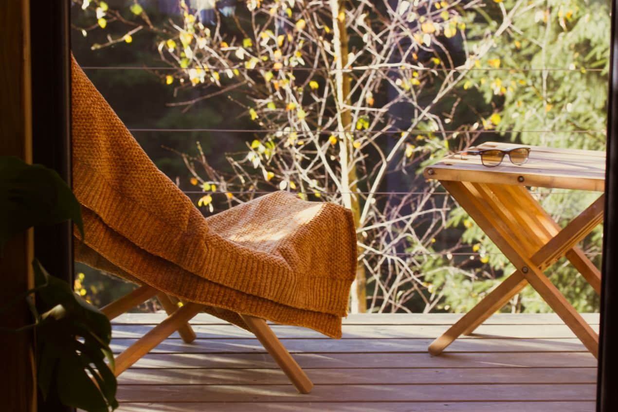 Holzstuhl mit Decke auf Balkon vor Waldkulisse – ideale Ruheoase, die mit blumenkästen perfekt abgerundet werden kann
