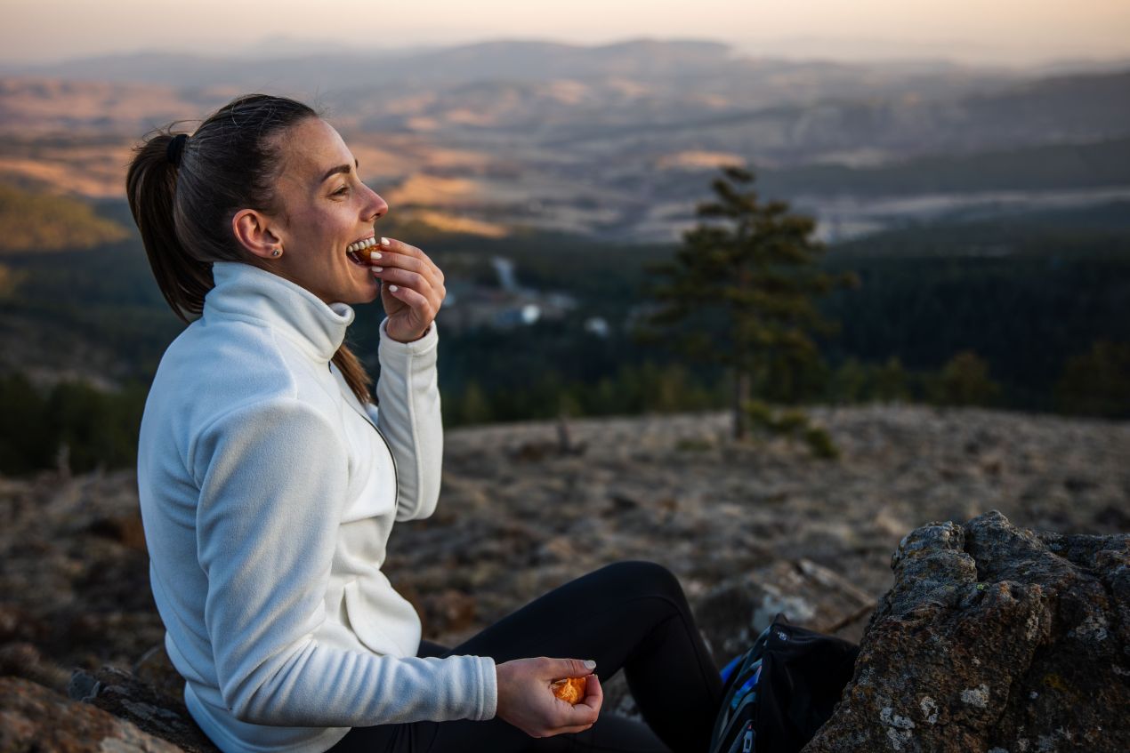 Wanderin regeneriert bei Sonnenuntergang mit Snack – Ernährung und Omega-3 Algenöl unterstützen die Erholung nach der Tour.